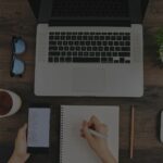 A freelancer's workspace with a laptop, notebook, pen, and phone, showcasing the tools needed for freelance writing success.